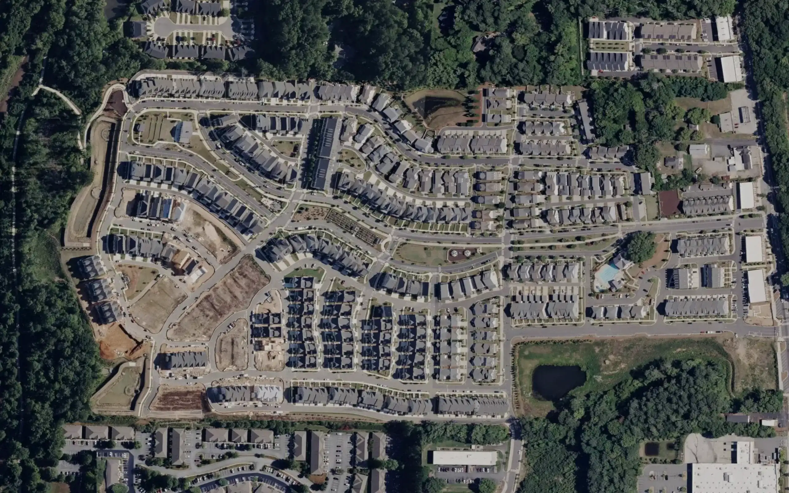 Satellite view of a residential community of townhomes and houses on curving streets, with a dashed line drawn around it.