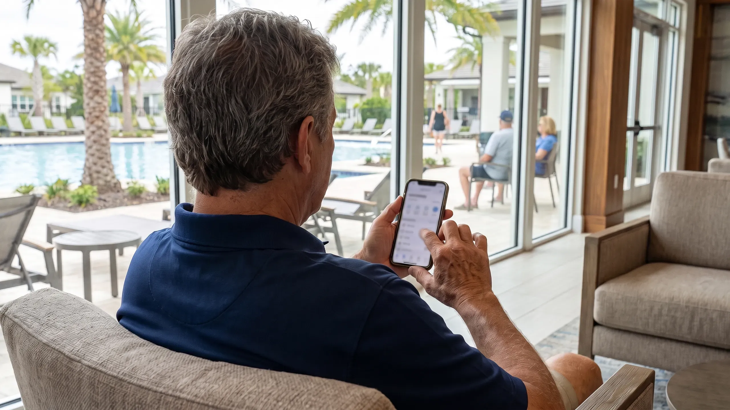 A board member in a clubhouse lounge chair seen from behind holds a phone showing a blurred ballot, the community pool and palms through floor-to-ceiling windows.