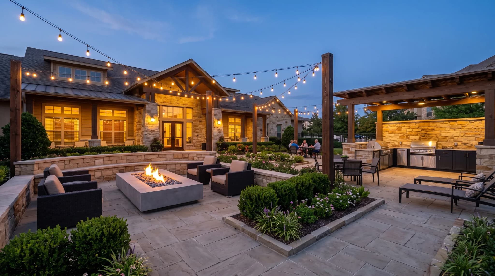 A covered clubhouse patio with a fire table, grills and seating. Residents sit at a table in the middle distance, faces indistinct.